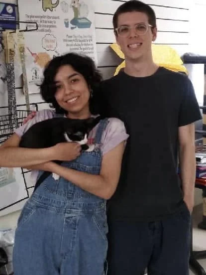 Melody holding kitten Midna at the shelter, with Chad standing beside them, both smiling.